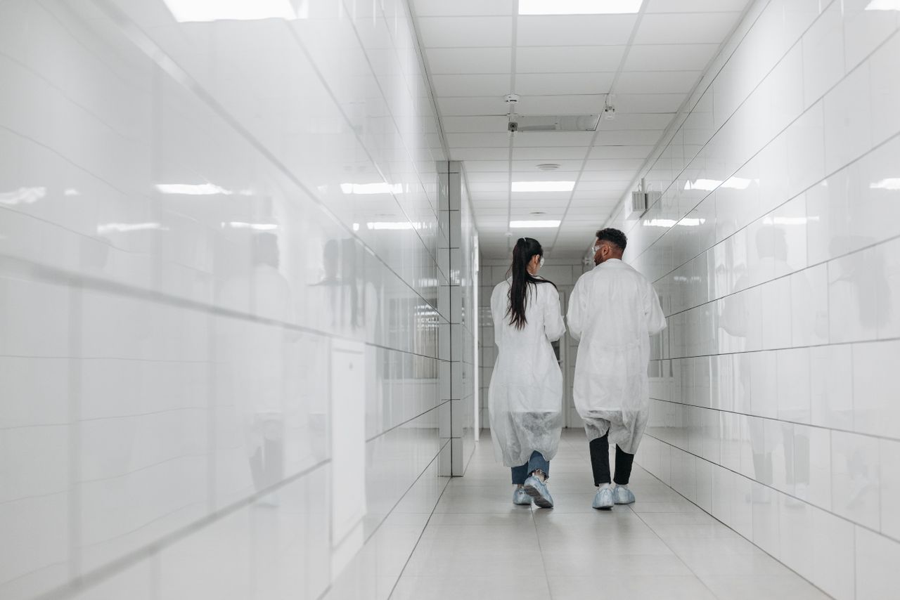 Two scientists in lab coats walk down a bright, tiled hallway, showcasing modern research environment.