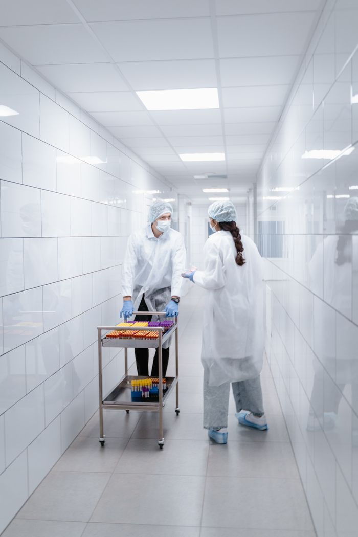 Two scientists in protective clothing handling vials in a lab hallway.